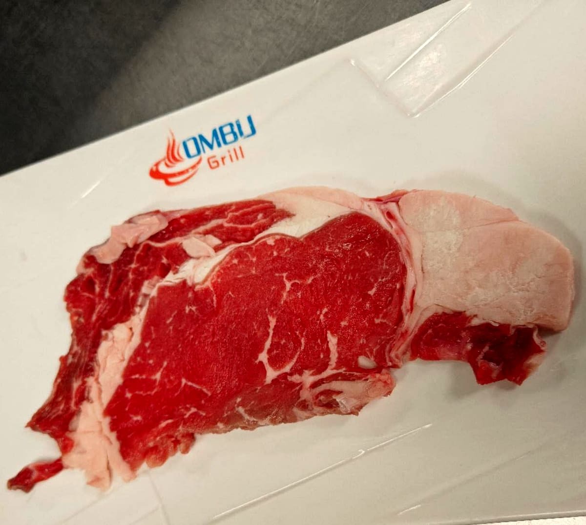 Raw ribeye steak on an Ombu Grill plate, ready for the table-side grill